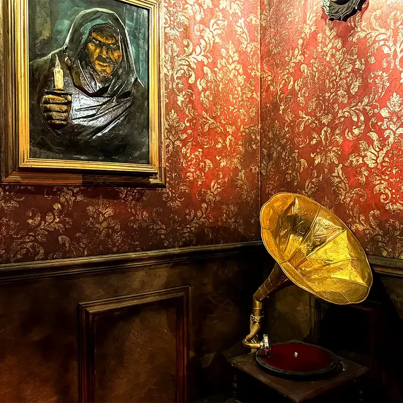 Detailaufnahme aus dem Escape Room Adams bei Final Escape Zürich mit unheimlichem Gemälde, roter Tapete und goldenem Grammophon.